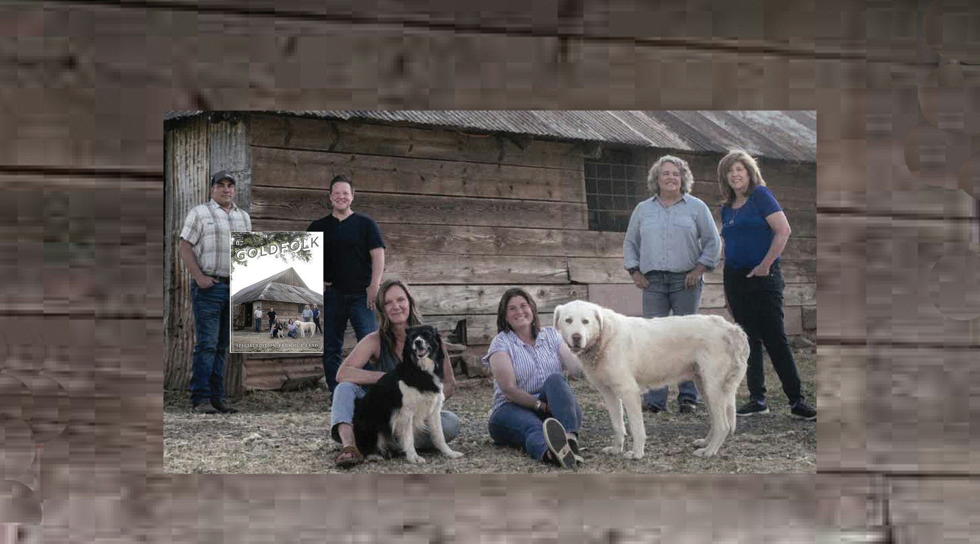 Group of six people and two dogs in front of a rustic wooden building.