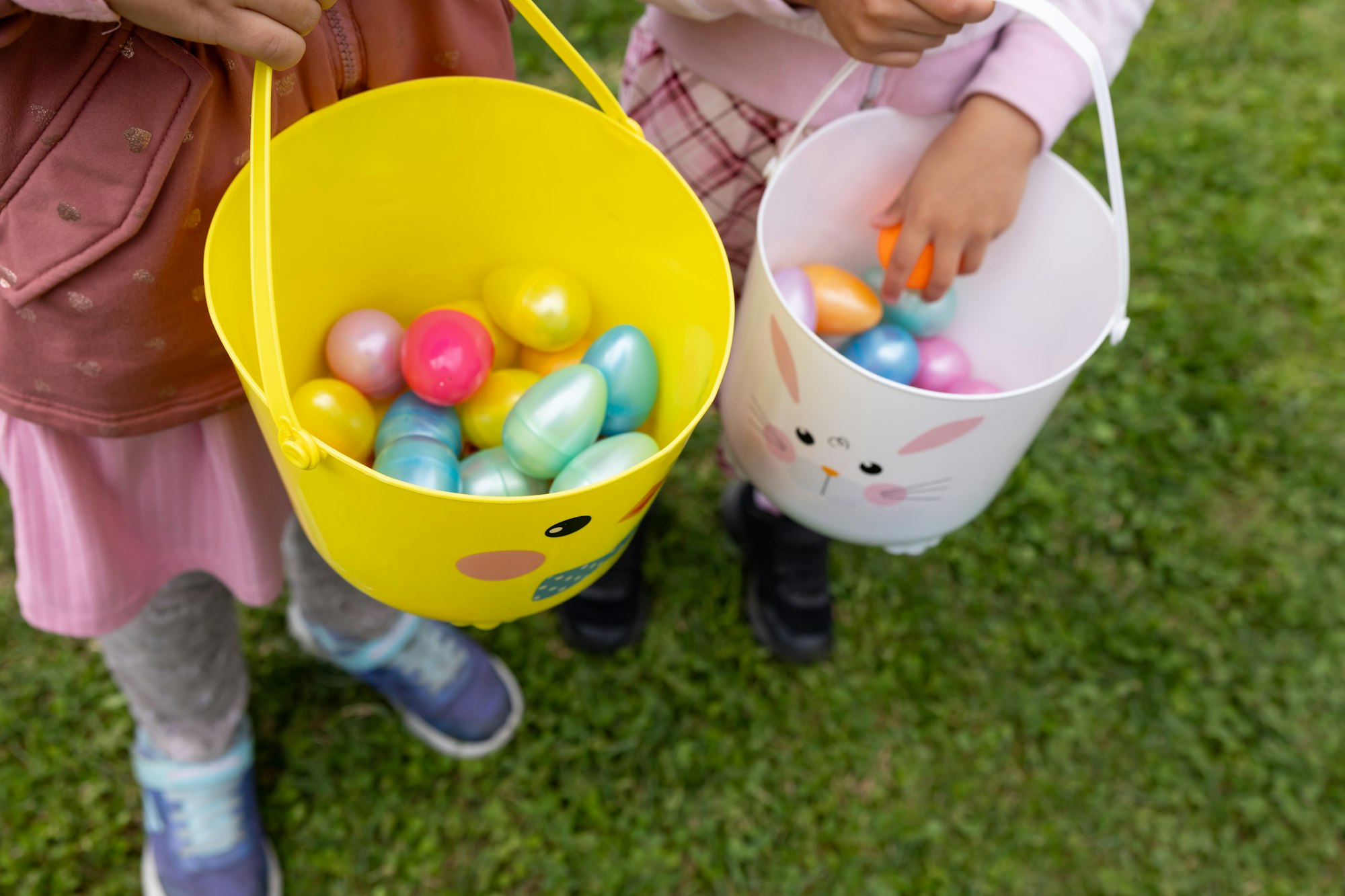 Two kids holding colorful Easter eggs in yellow and white buckets with bunny designs.