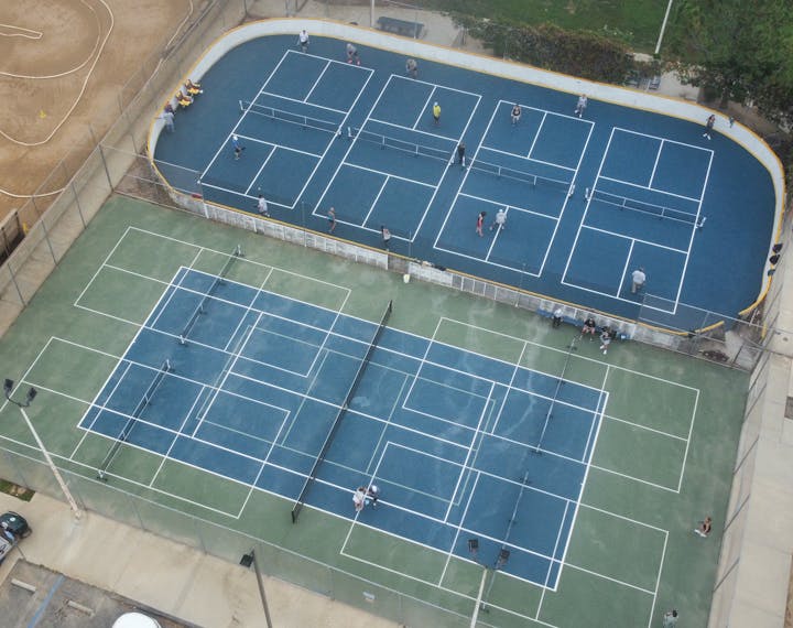 Aerial view of tennis courts with players and adjacent walking paths.