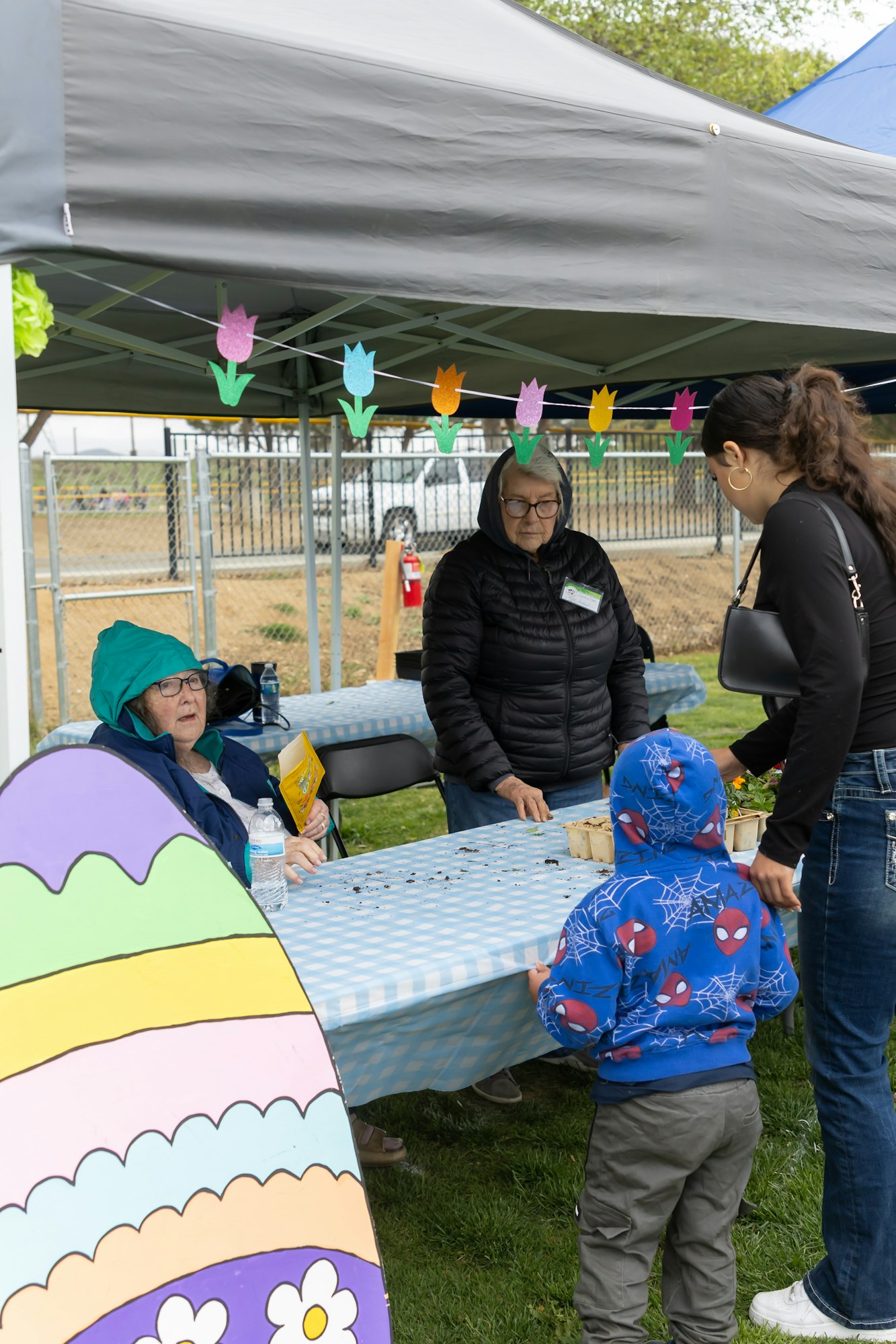 People at an outdoor event tent with Easter decorations and a child in a blue hoodie.