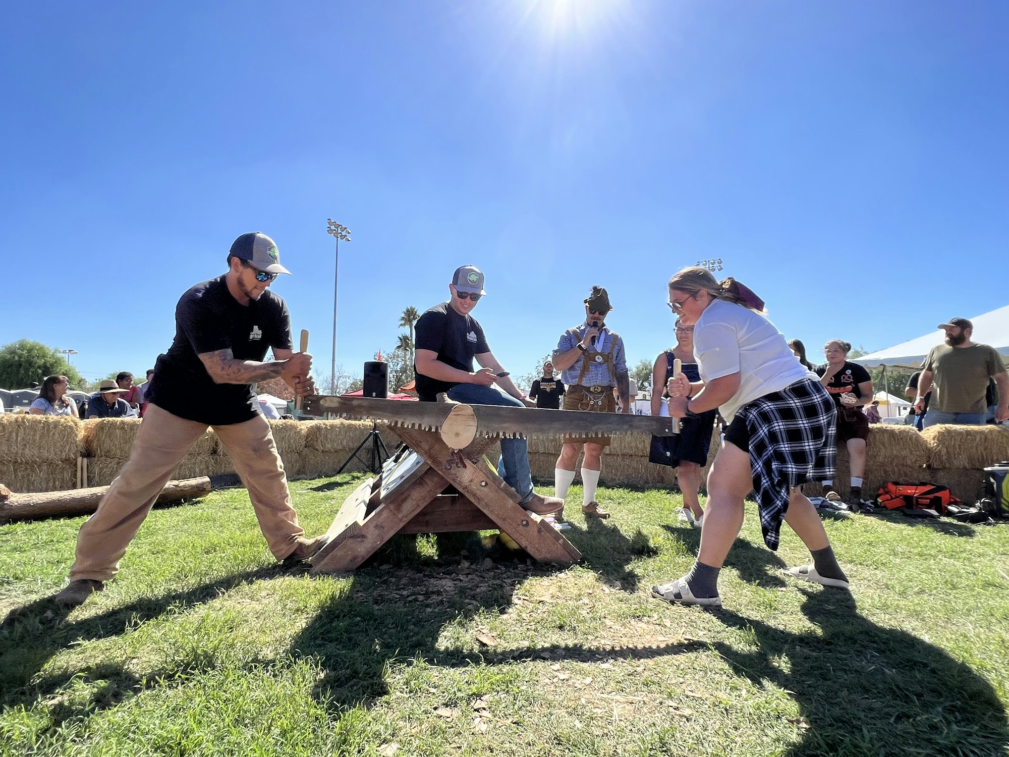 Two people using a crosscut saw at an outdoor event with onlookers.