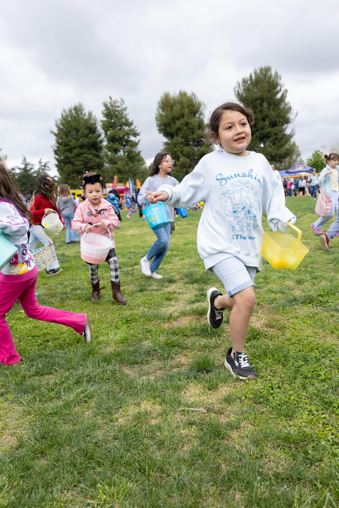 Children running on grass with baskets during an outdoor event.