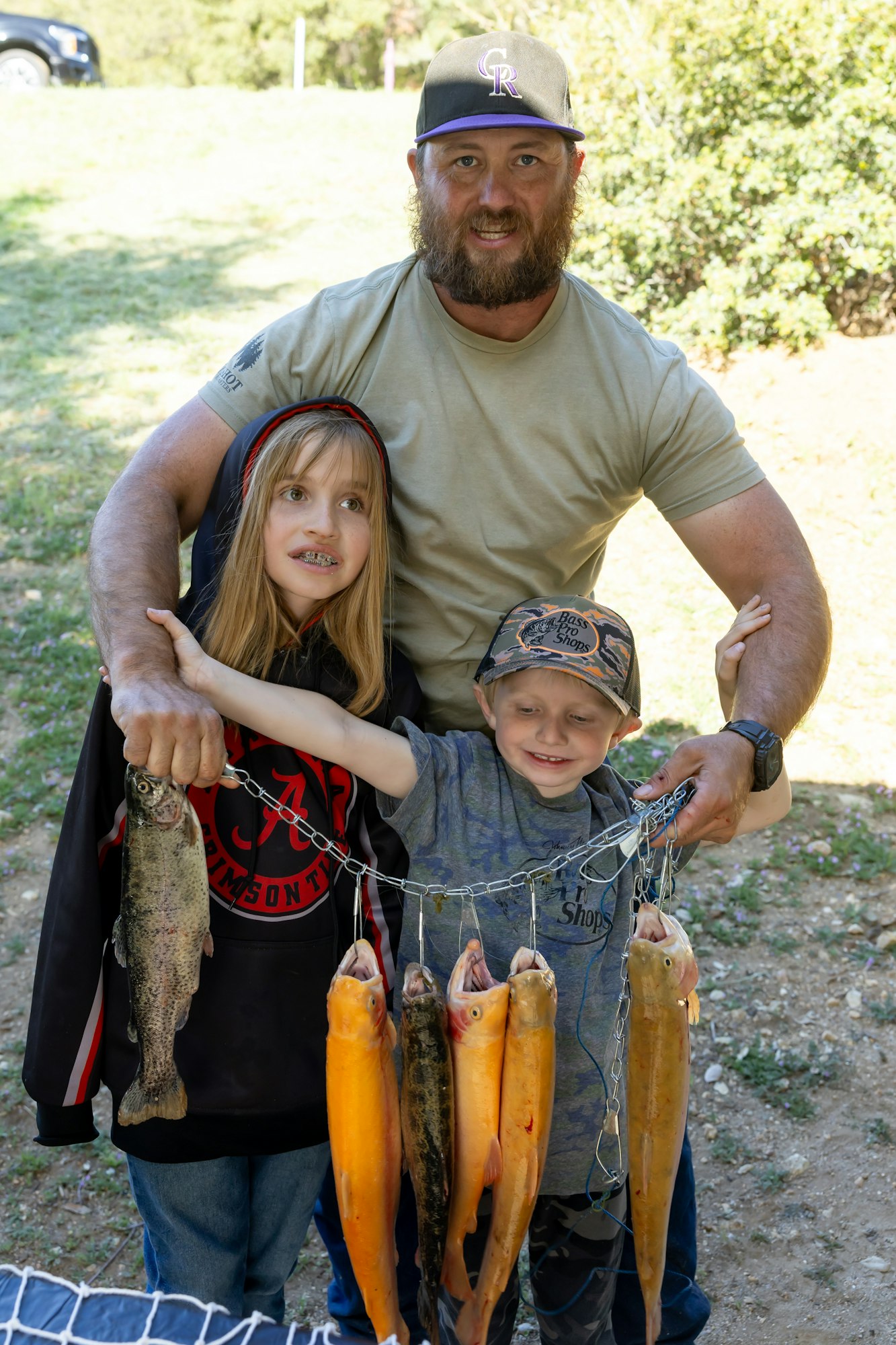Three people smiling while holding a line with multiple fish outside.