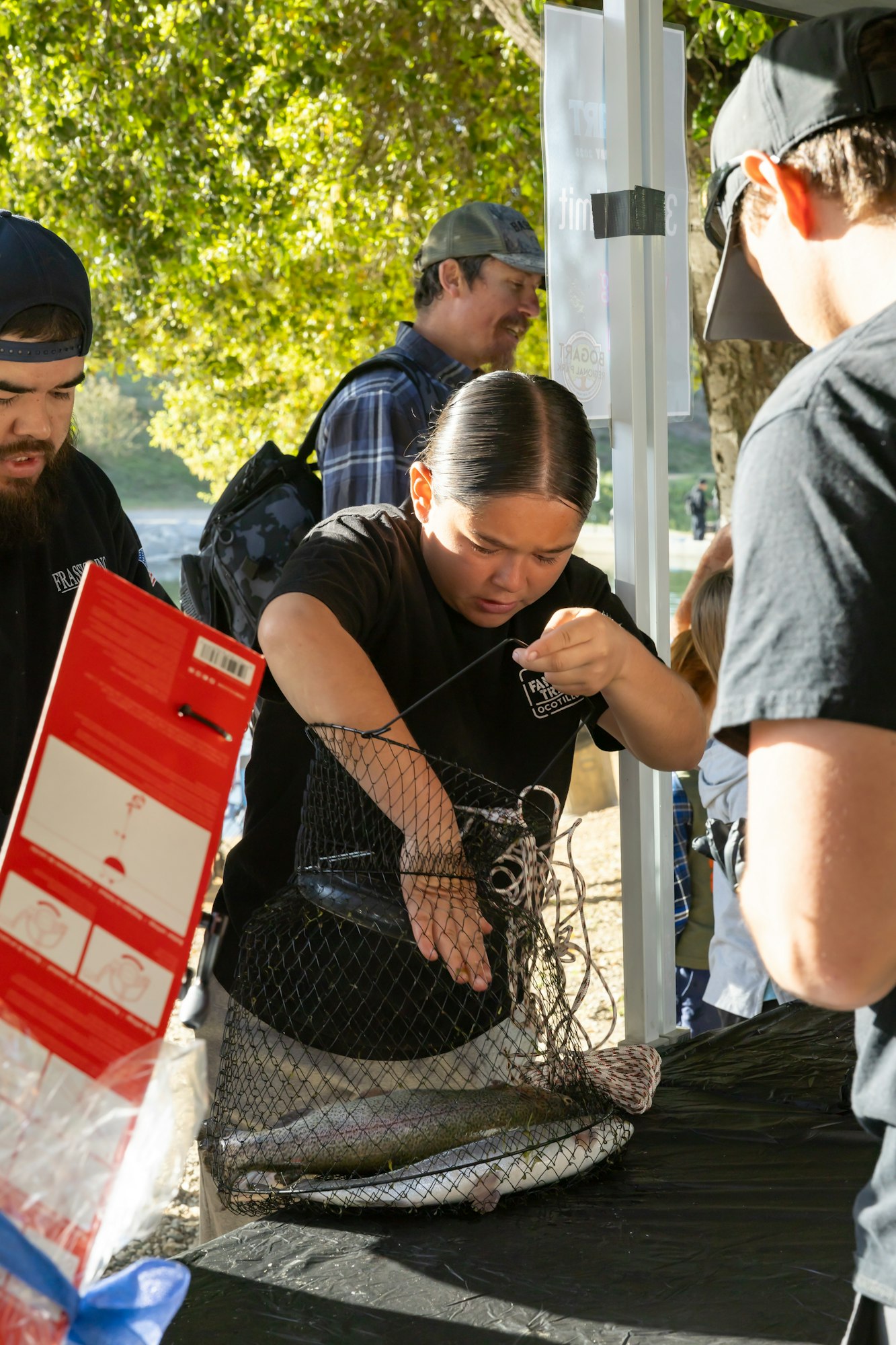 People are inspecting a fish inside a net at an outdoor event.