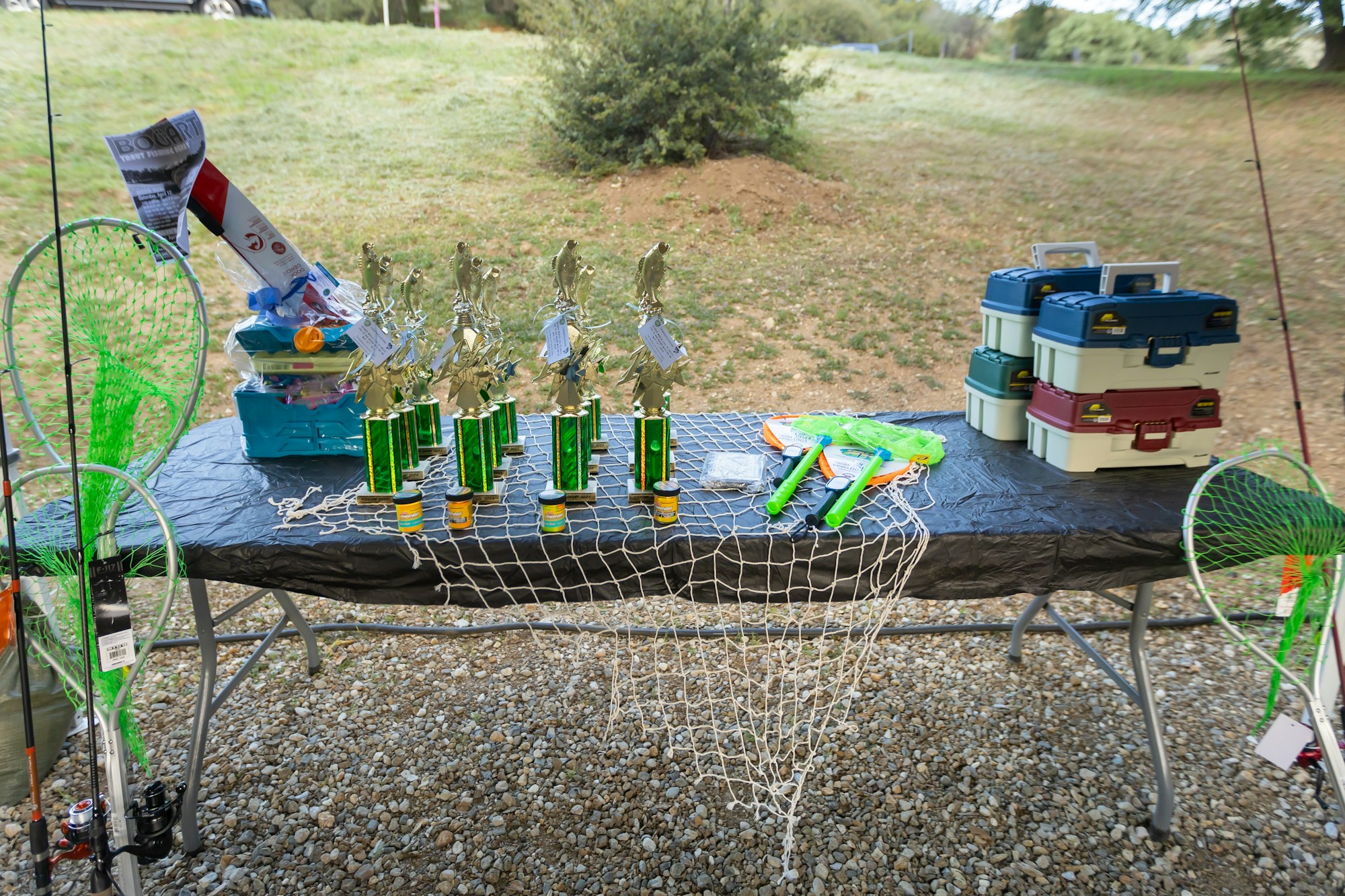 Trophies, tackle boxes, fishing nets, fishing rods, and other fishing gear on a table outdoors.