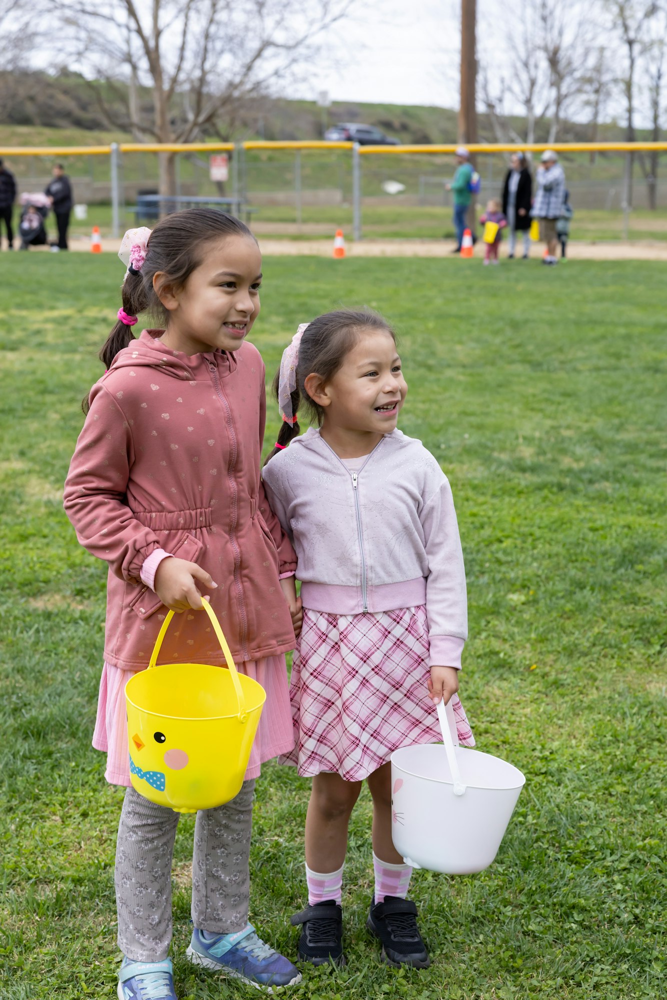 Two children outdoors holding yellow and white buckets, smiling, with a grassy background.