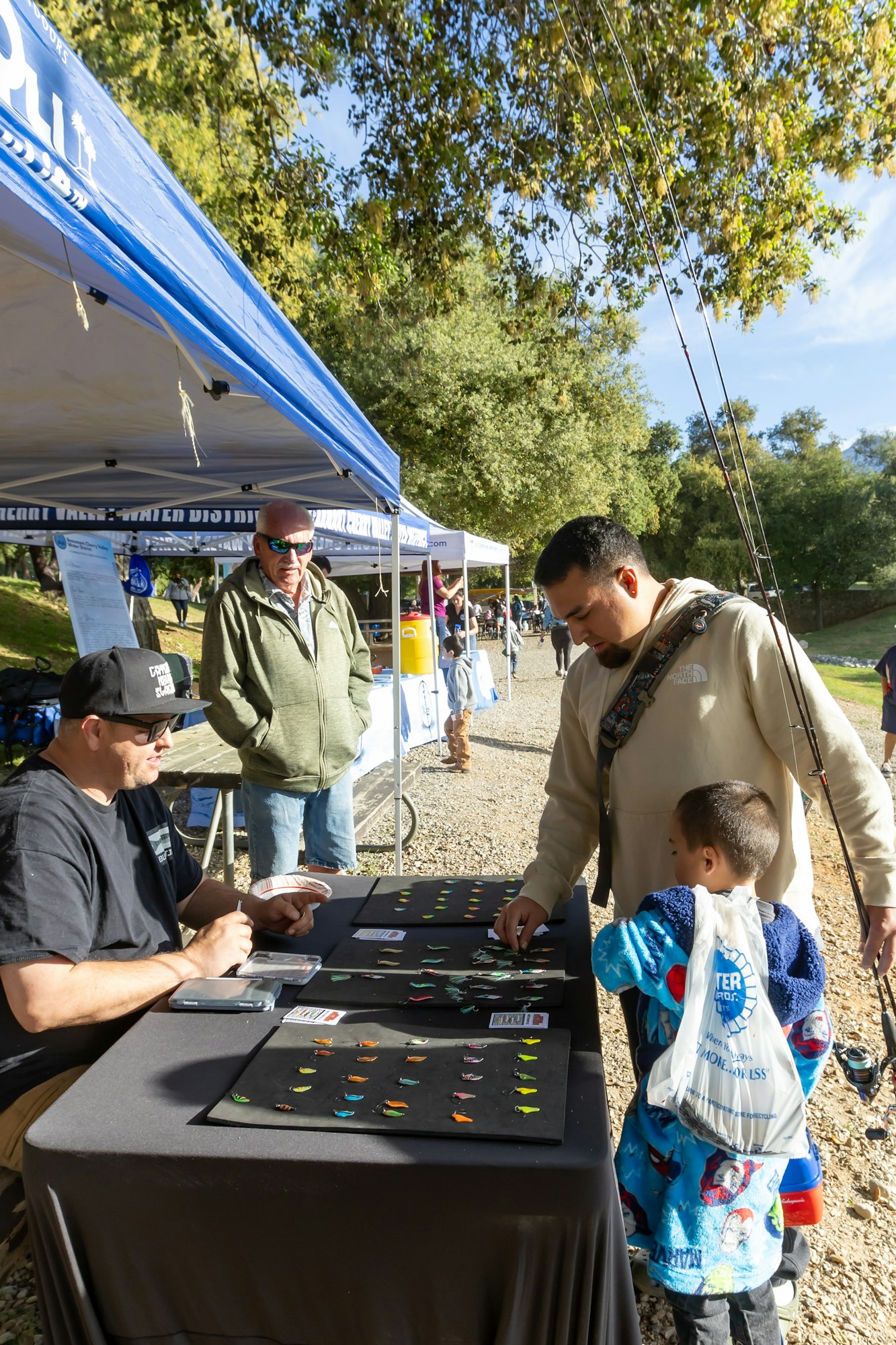 People at an outdoor booth selecting items on a table with colorful fish-shaped pieces under a canopy.
