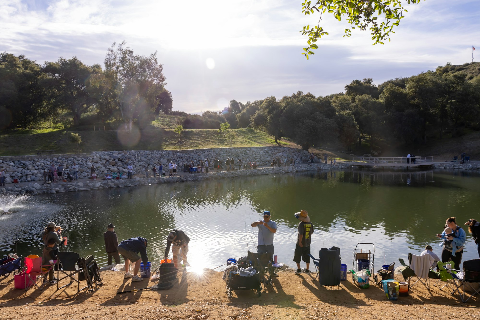 May contain: nature, outdoors, scenery, pond, water, person, clothing, hat, summer, footwear, shoe, chair, furniture, lake, shorts, accessories, bag, and handbag