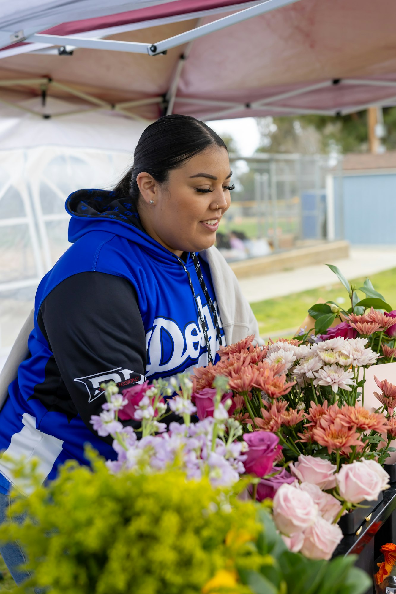A person in a blue hoodie arranging colorful flowers under a canopy.