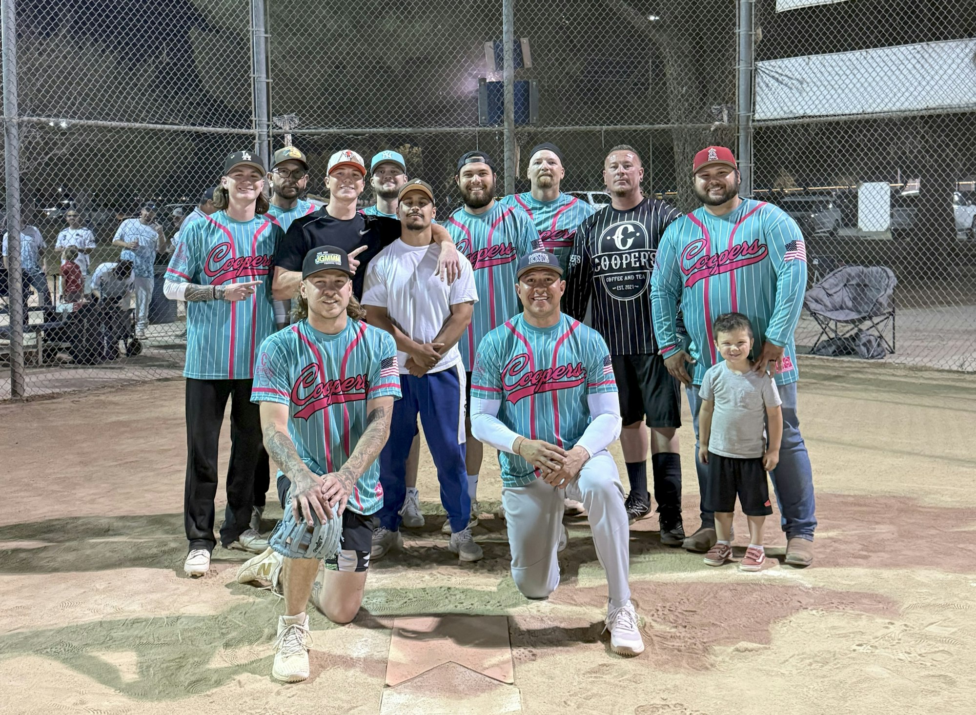 A group of people in baseball uniforms posing on a baseball field at night.