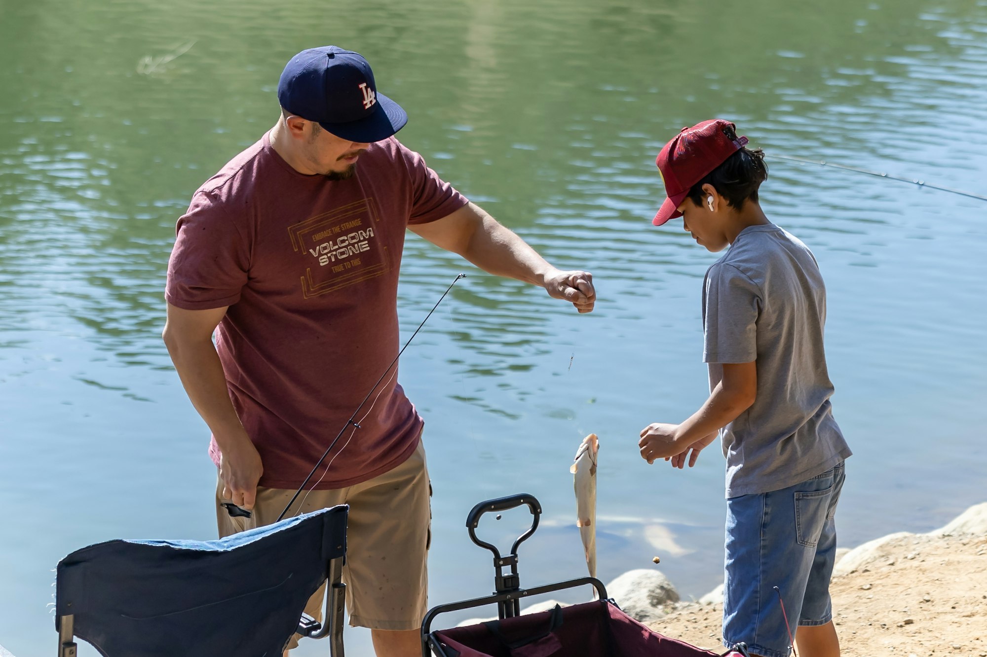 Two people fishing by a lake, holding a caught fish.