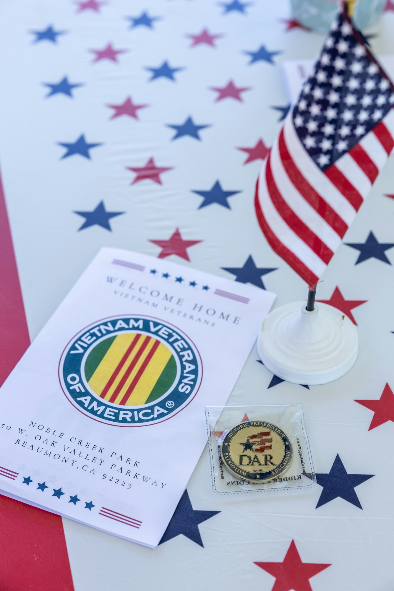 The image features a patriotic table setup with an American flag, a welcome brochure for Vietnam veterans, and a DAR medal.