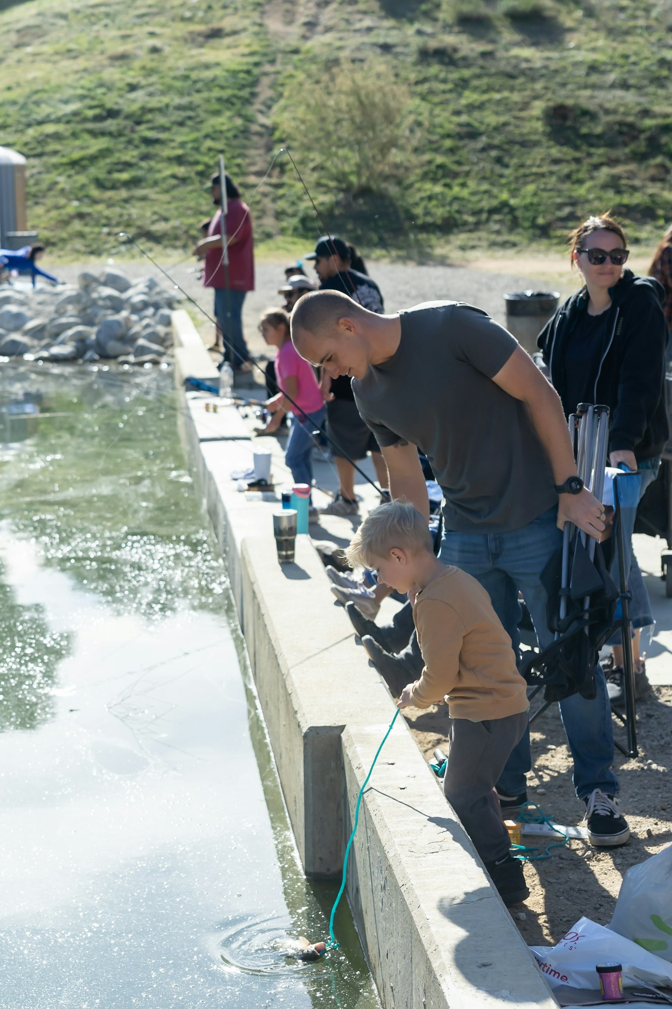 A group of people, including a child, fishing by a water's edge with rods and equipment.