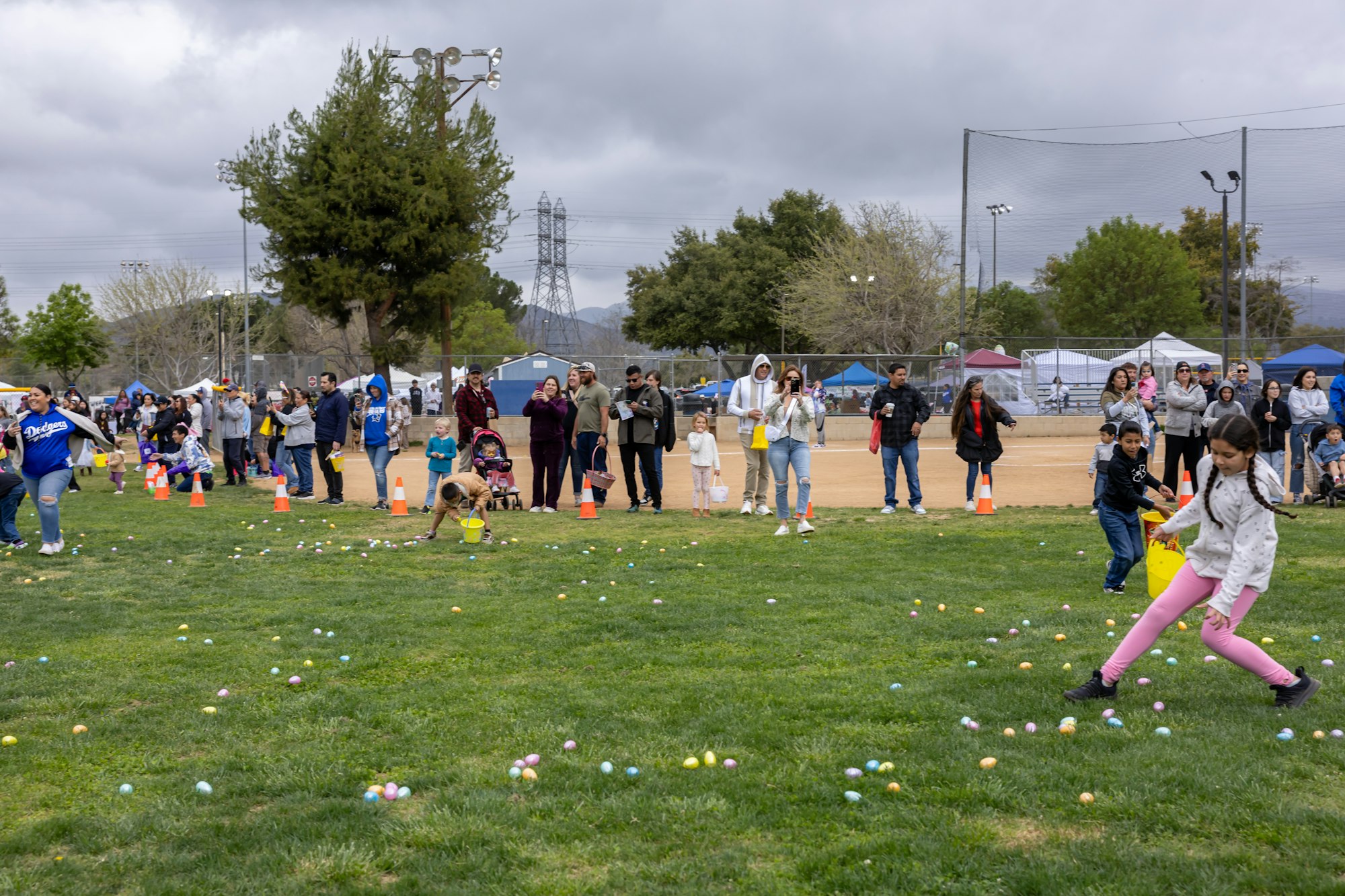 A group of people, including adults and children, participate in an Easter egg hunt outside on a cloudy day.