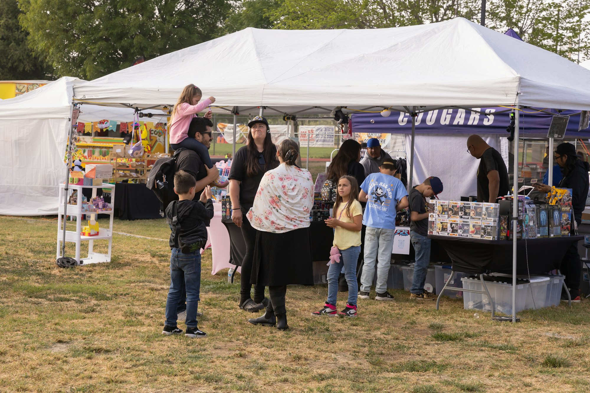 People browsing stalls at an outdoor market or fair, with merchandise displayed under tents.