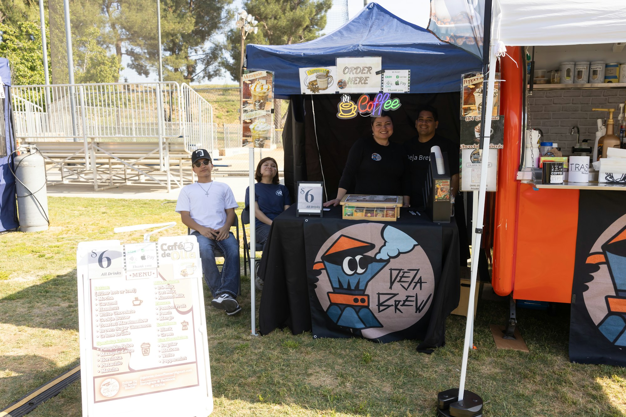 A coffee stand at an outdoor event with people, a menu, and a "Deja Brew" sign.