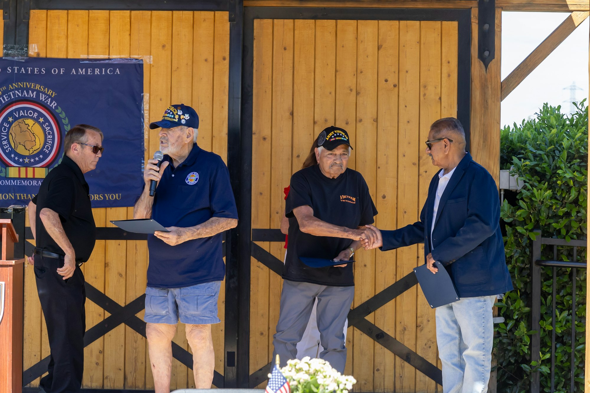 The image shows a commemorative event for Vietnam War veterans, featuring award presentations and handshakes.