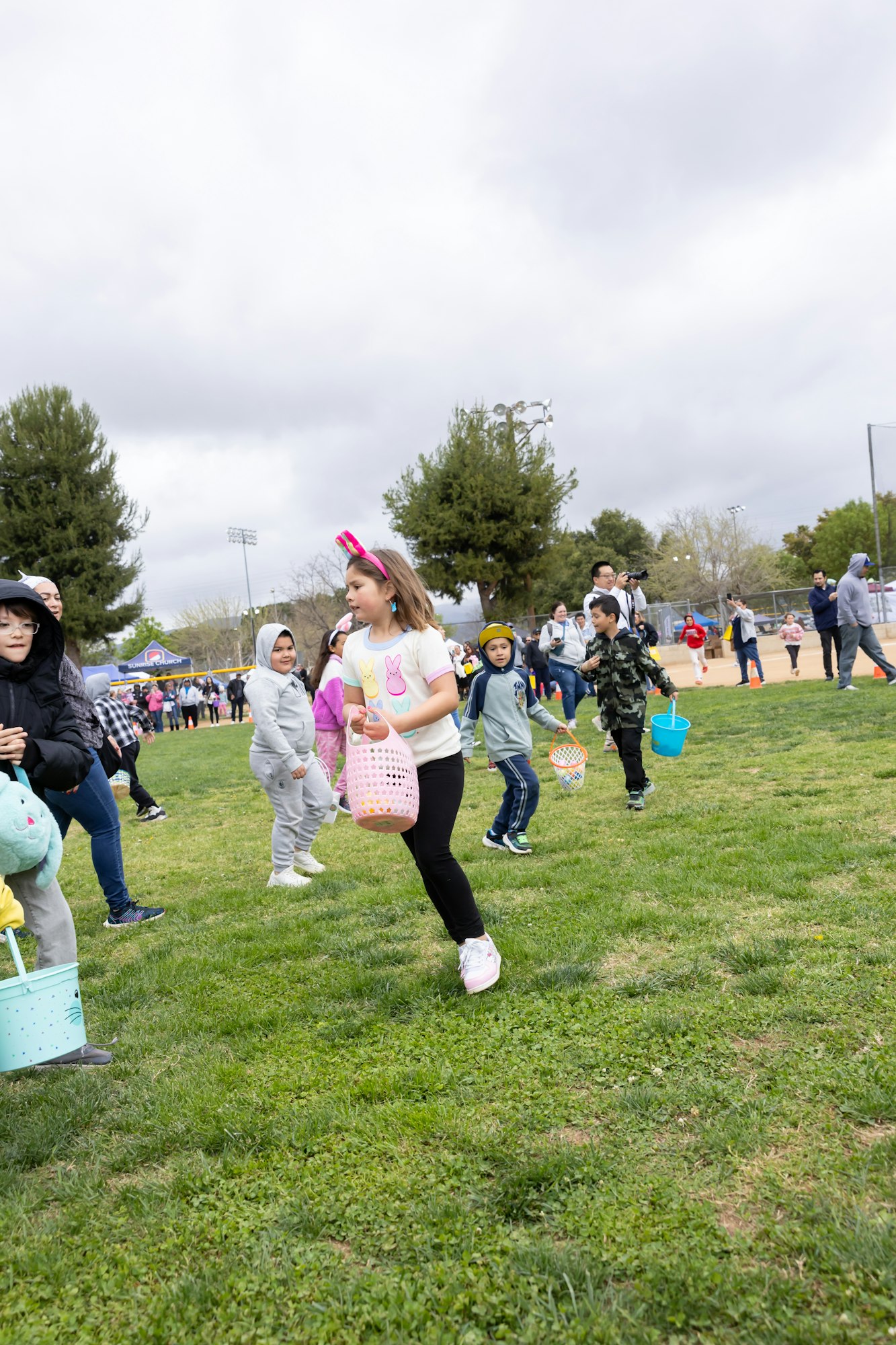 Children with baskets participate in an outdoor egg hunt event on a grassy field.