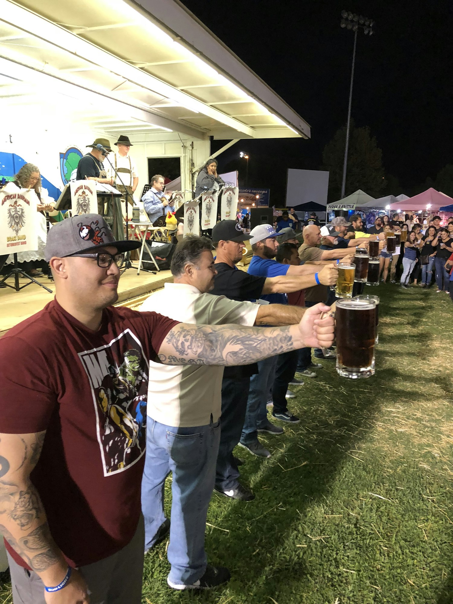 People are participating in a beer-holding contest at an outdoor event, standing in a line with large mugs.