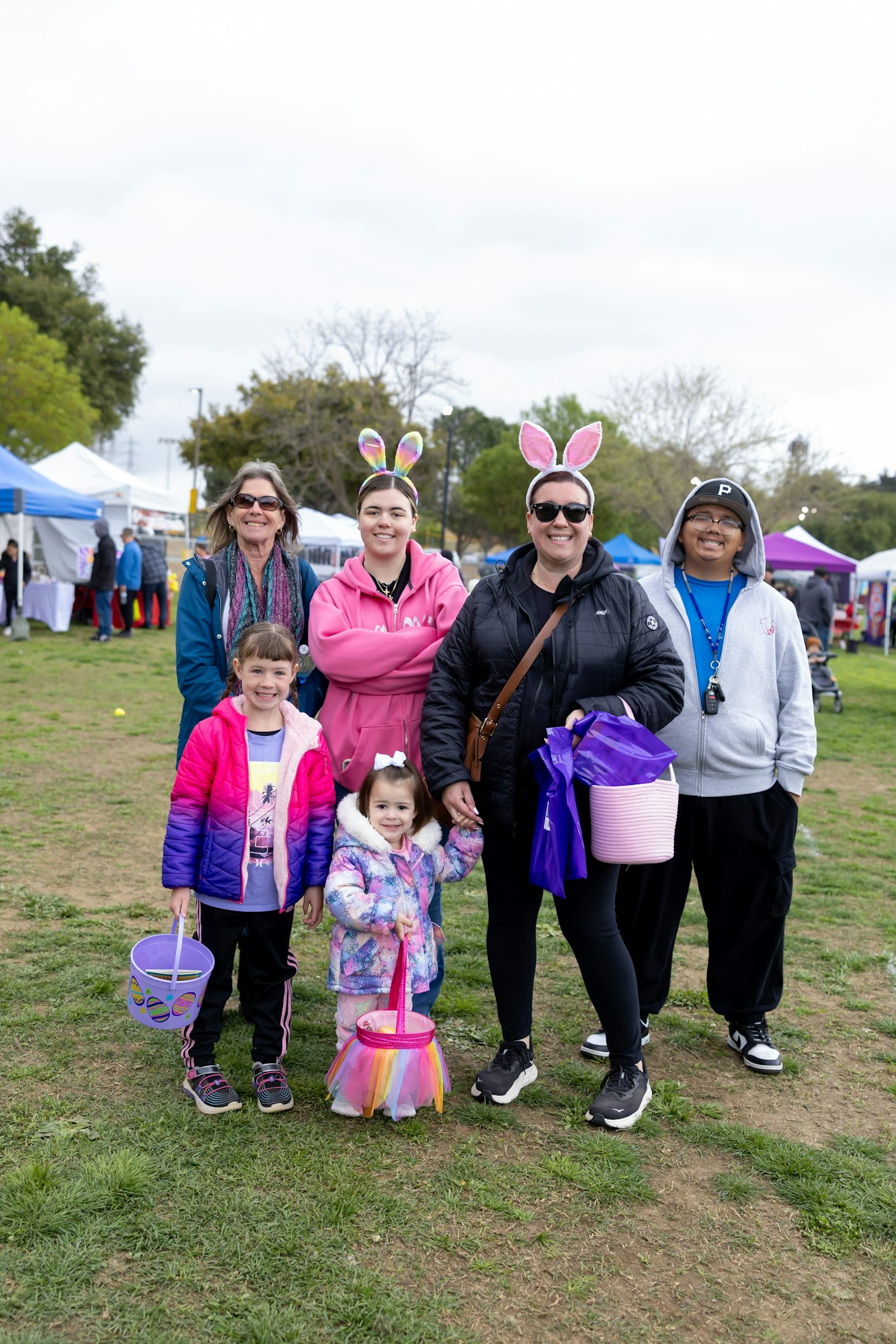 A group of people, some wearing bunny ears, holding baskets at an outdoor event with tents in the background.