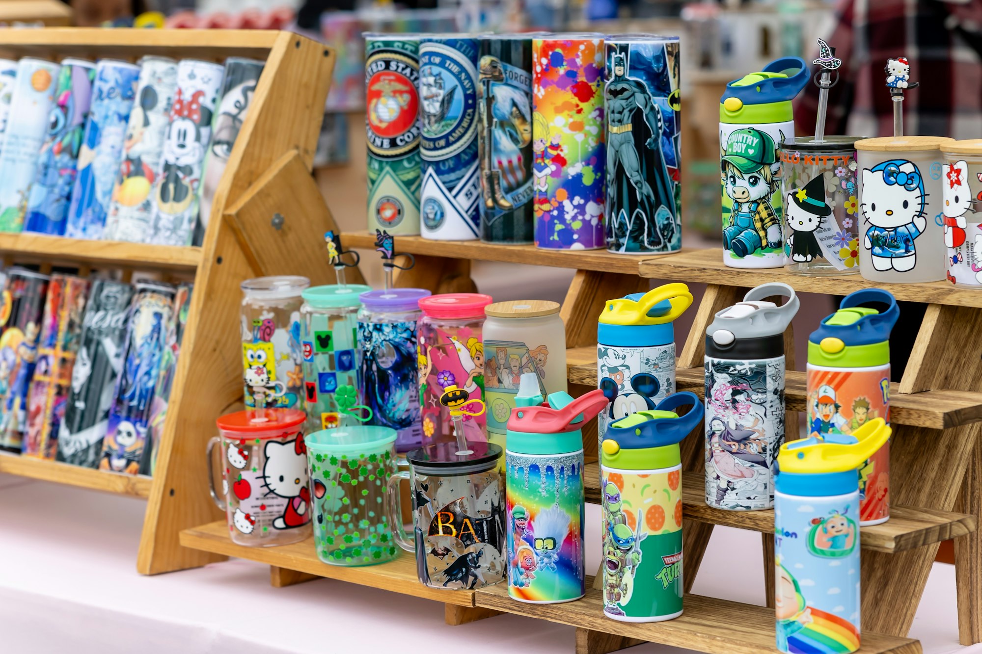 Colorful water bottles and tumblers with cartoon and pop culture designs displayed on wooden shelves.