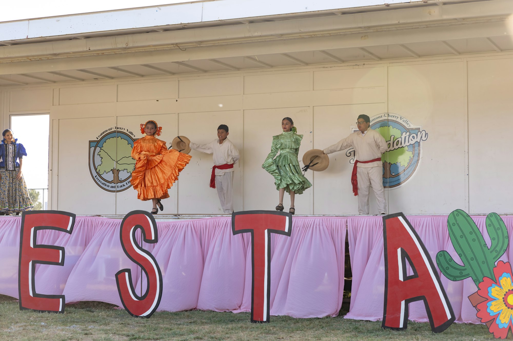 Dancers in colorful outfits performing on stage with "FIESTA" letters in front.
