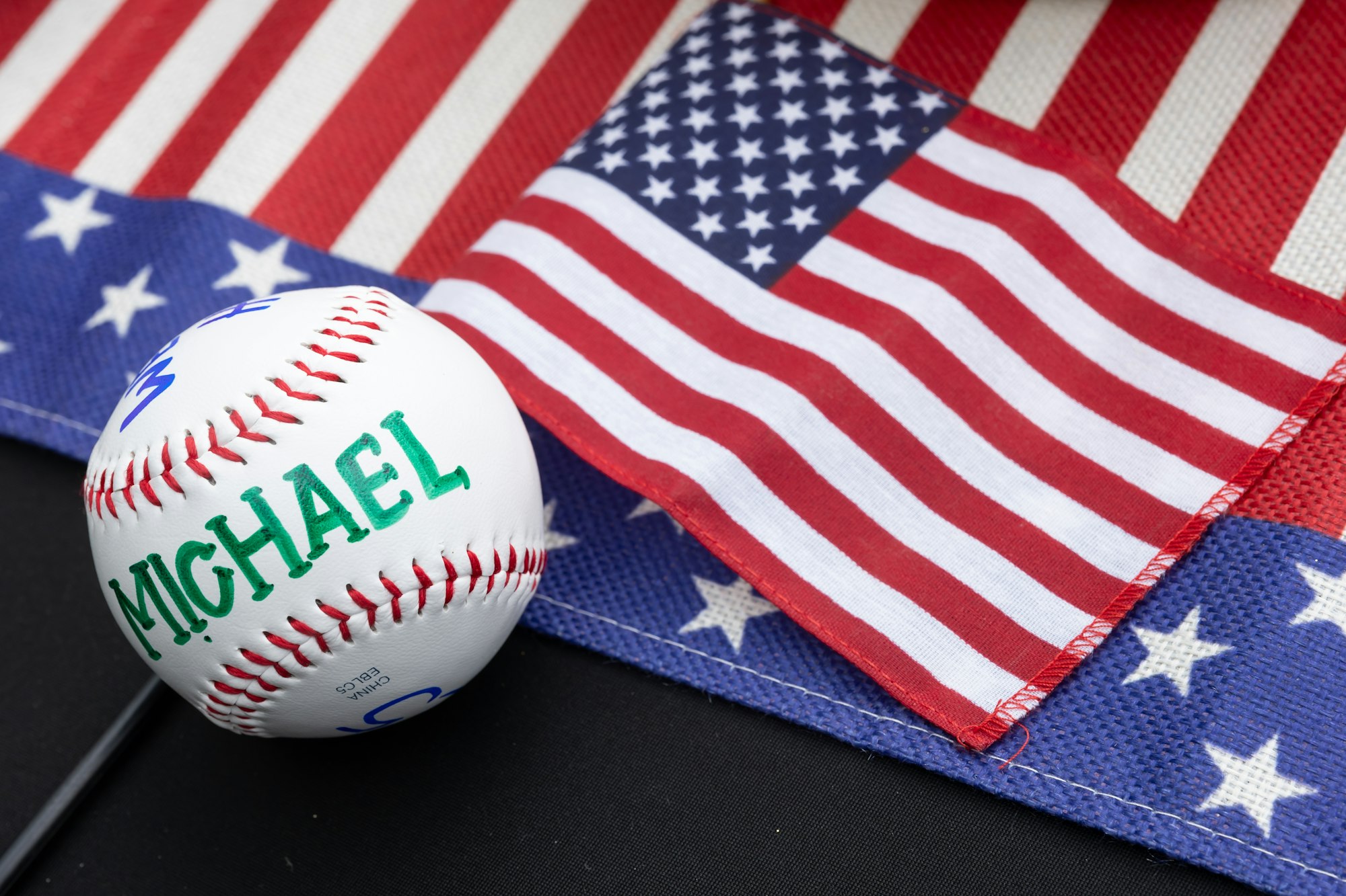 A baseball with "Michael" written on it lies next to an American flag.