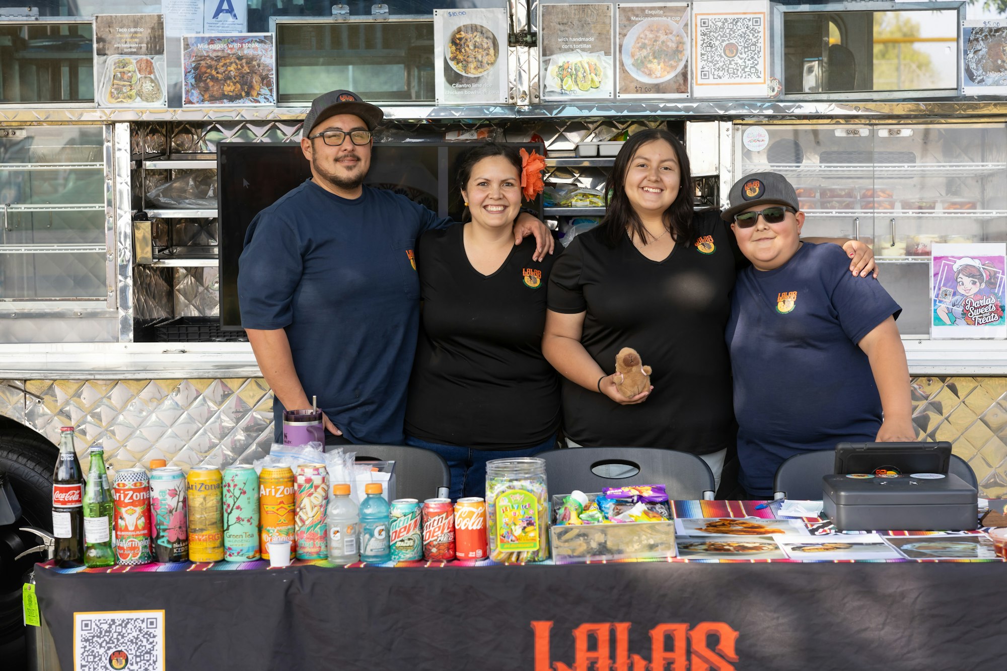 Four people smiling in front of a food truck with snacks and drinks on a table.