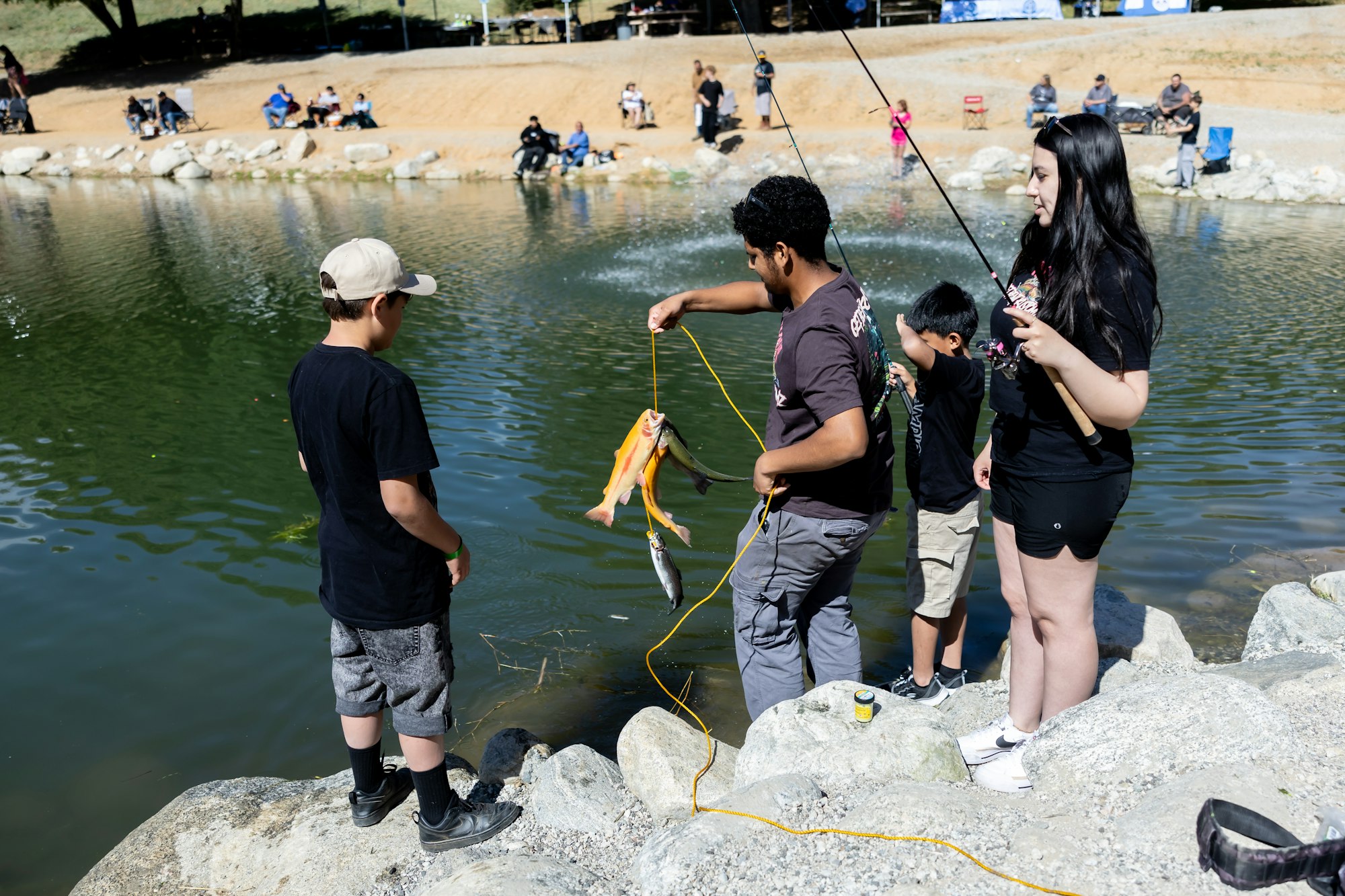 Group of people fishing by a pond; one person is holding multiple fish on a string.