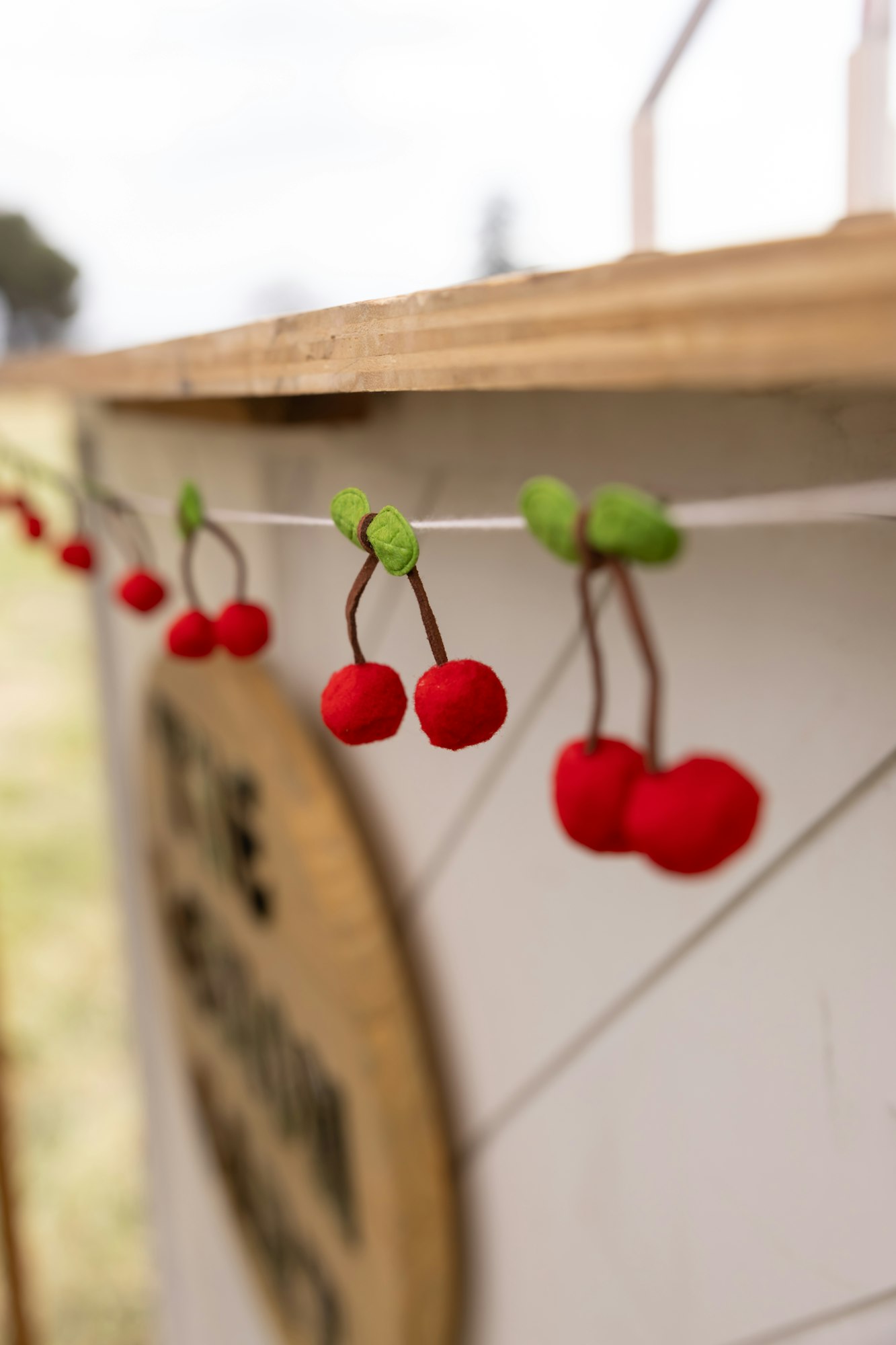 String of felt cherry decorations hanging on a wooden surface.