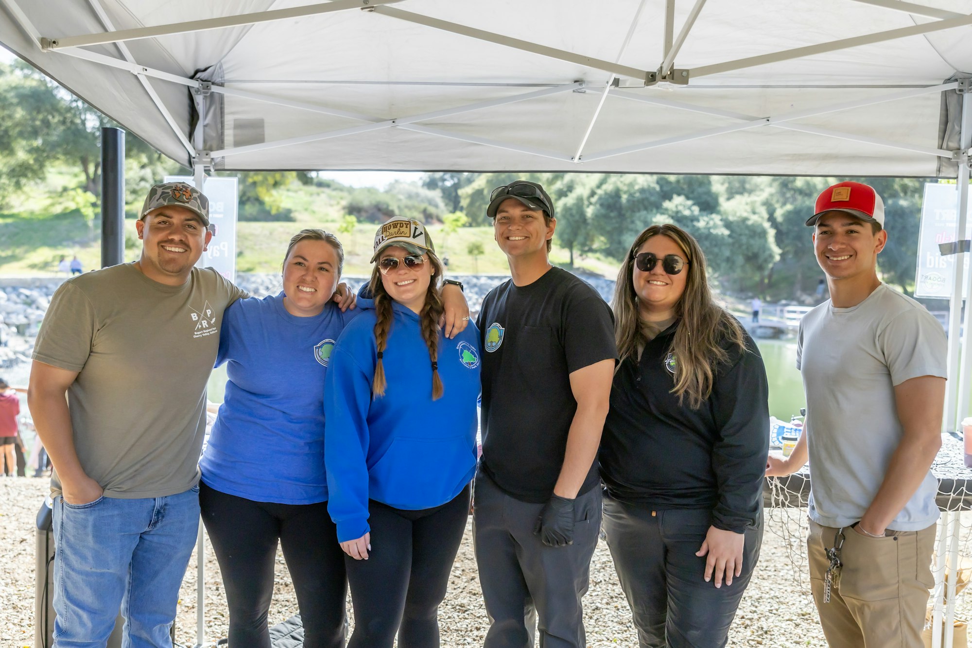 A group of six people smiling under a white canopy outside.