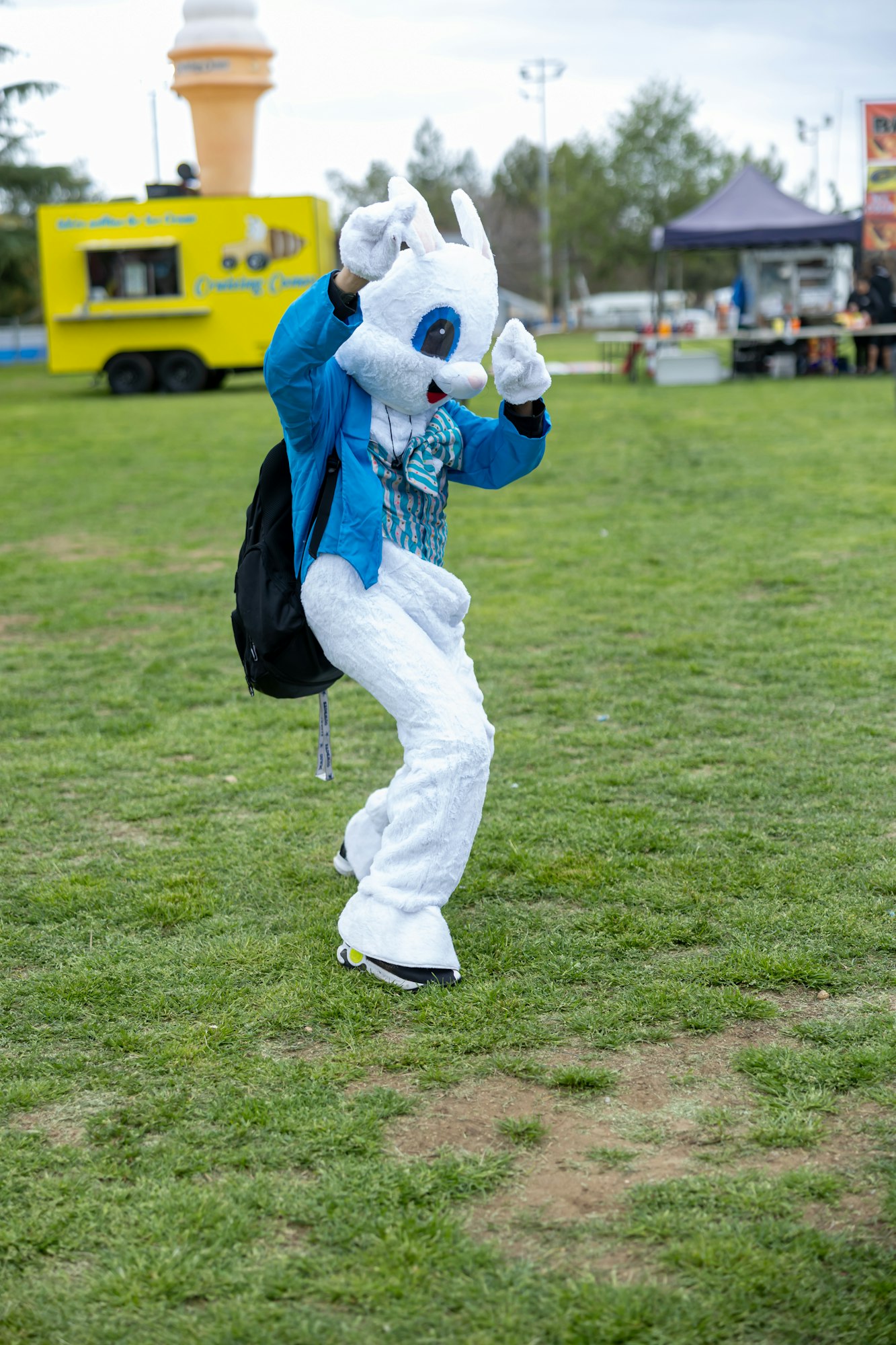 A person in a bunny costume dancing on grass, with a yellow ice cream truck in the background.