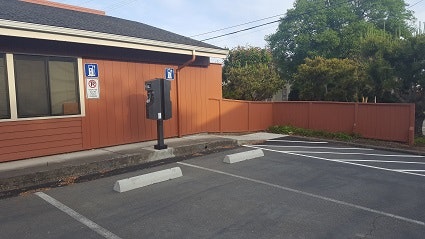 Photo may contain a picture of the NCUAQMD Charging Station. Brown building with windows. Charger is located in a parking lot.