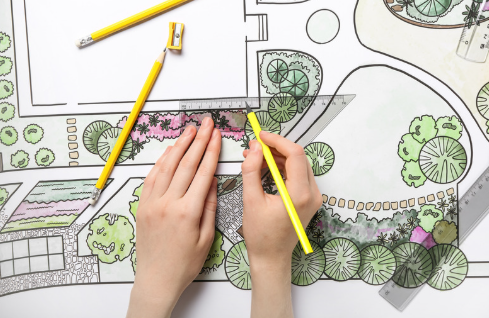 A person is sketching a garden layout using colored pencils and drawing tools on paper.