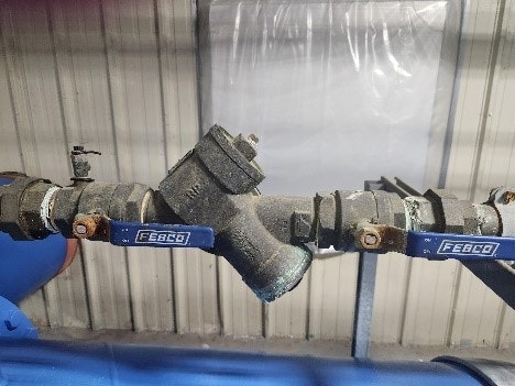 Industrial piping with valves and brackets against a metal wall.