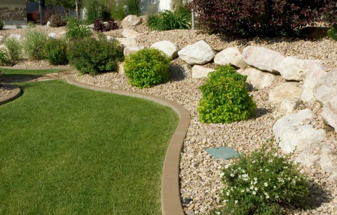 A landscaped garden featuring green grass, rocks, shrubs, and a curved pathway. Bright and well-maintained.