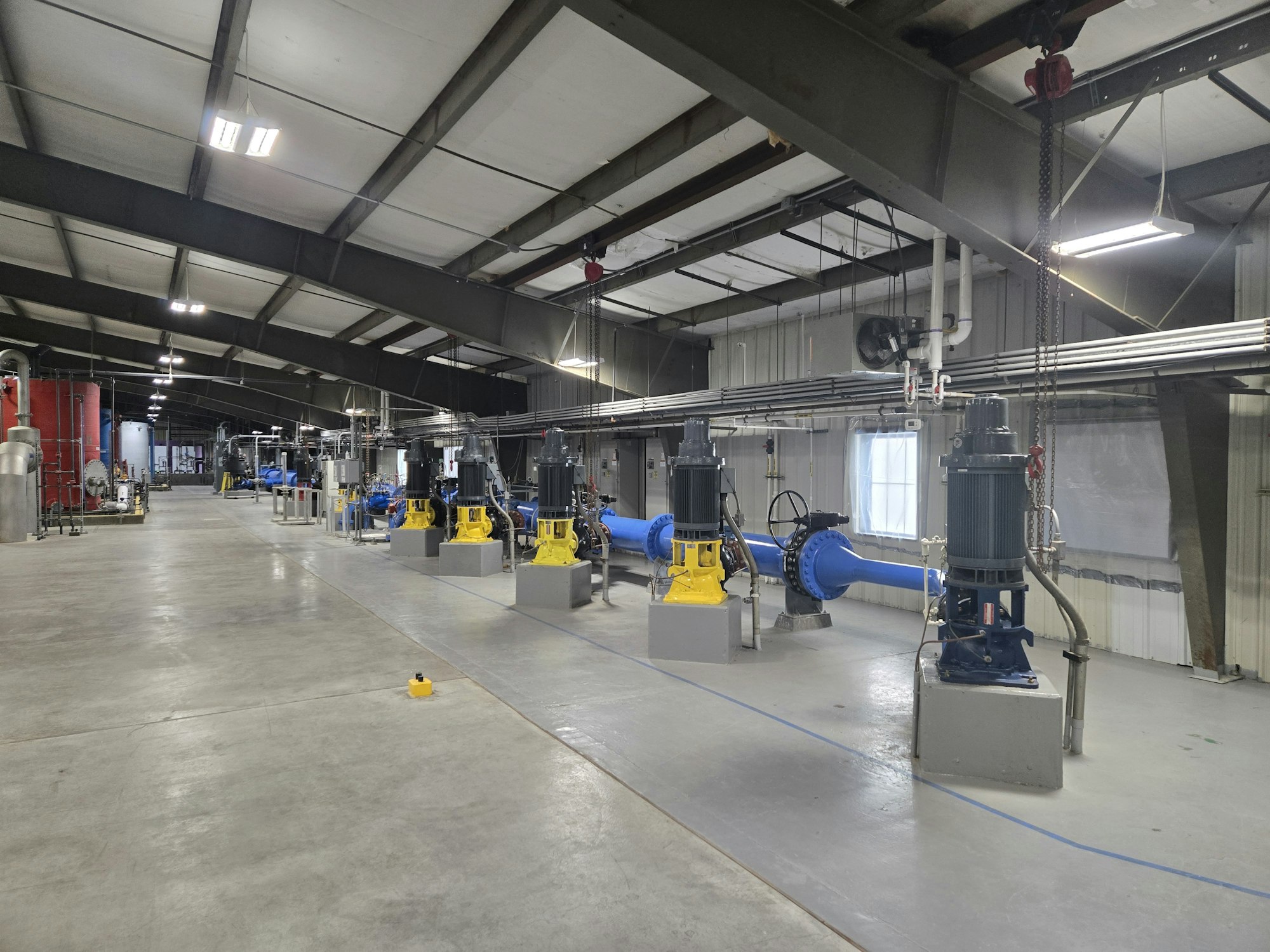 An industrial facility interior with machinery and equipment, including large pipes and motors, under a metal roof.