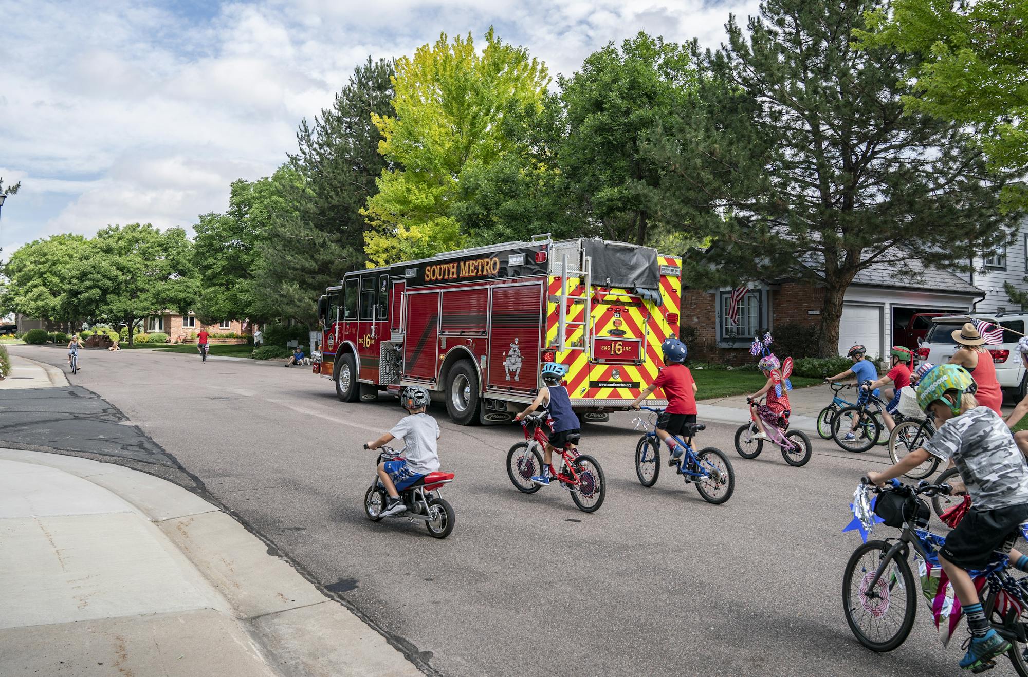 A fire truck and a group of kids riding decorated bikes on a suburban street.