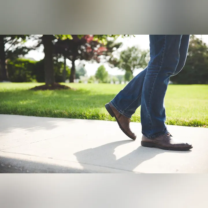 Person walking on a sidewalk with green grass and trees in the background.