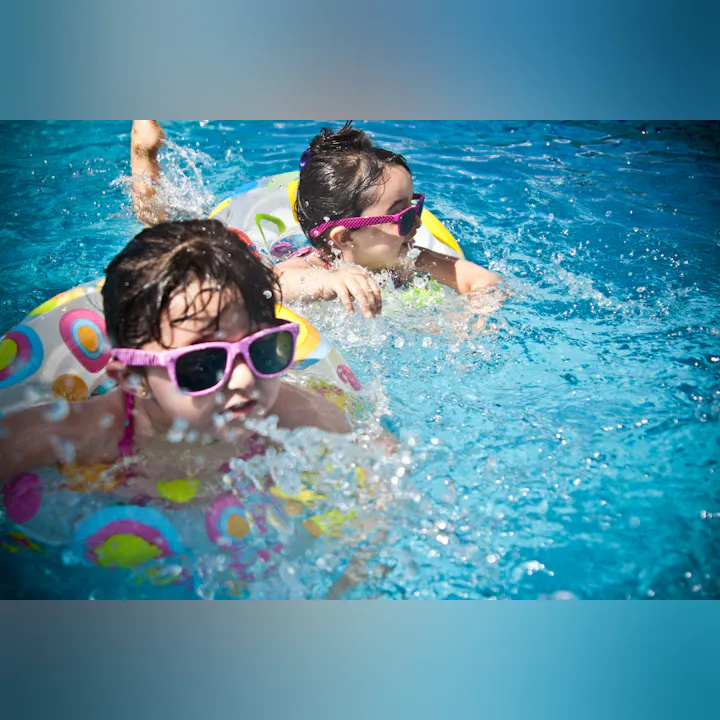 Kids with sunglasses playing in a pool using inflatable rings.