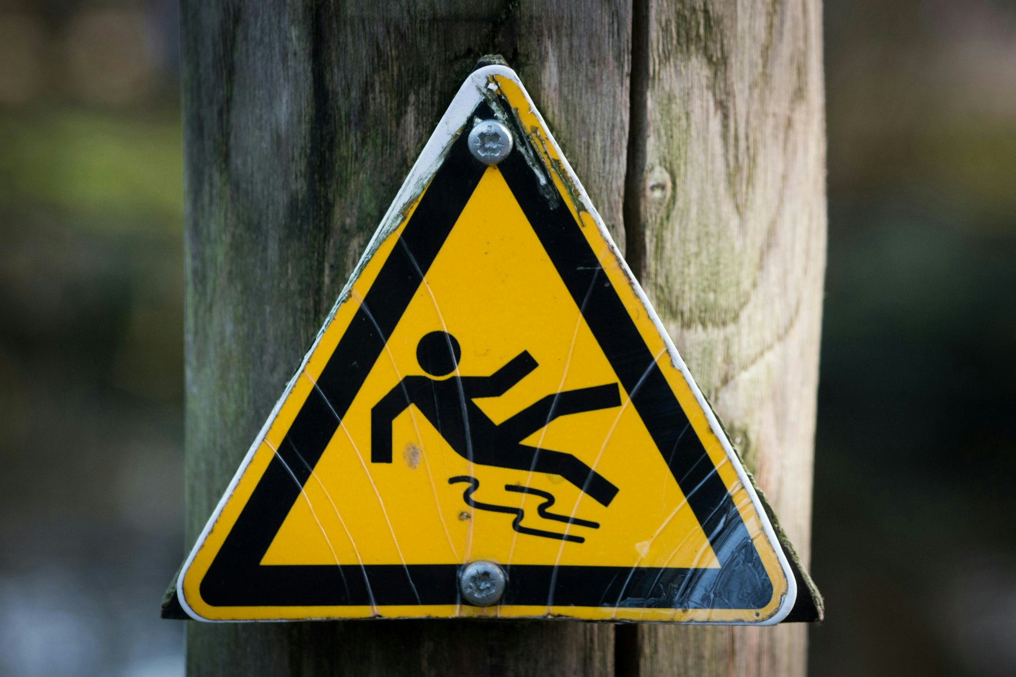 Yellow triangular warning sign for slippery surface attached to a wooden post.