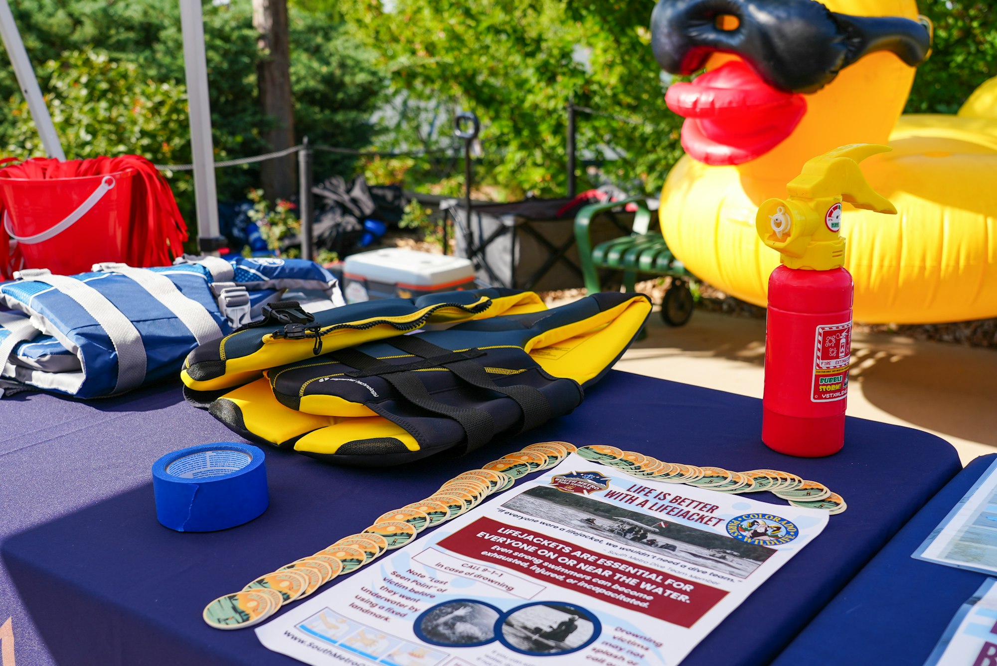 The image shows life jackets, a fire extinguisher, a poster promoting water safety, and a large inflatable duck in the background.