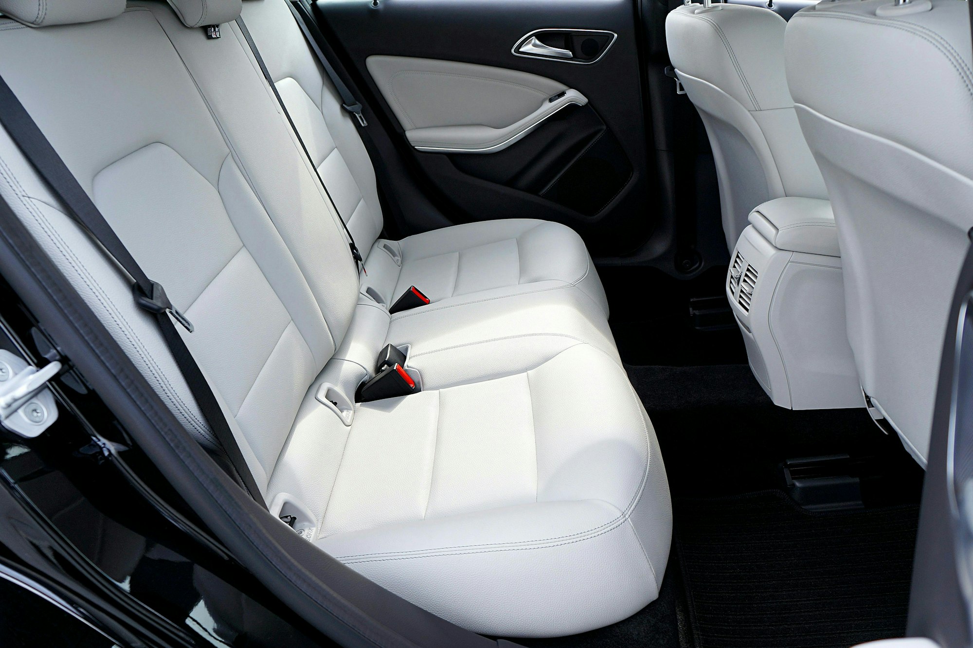A car's backseat interior with light-colored leather upholstery and seatbelts.