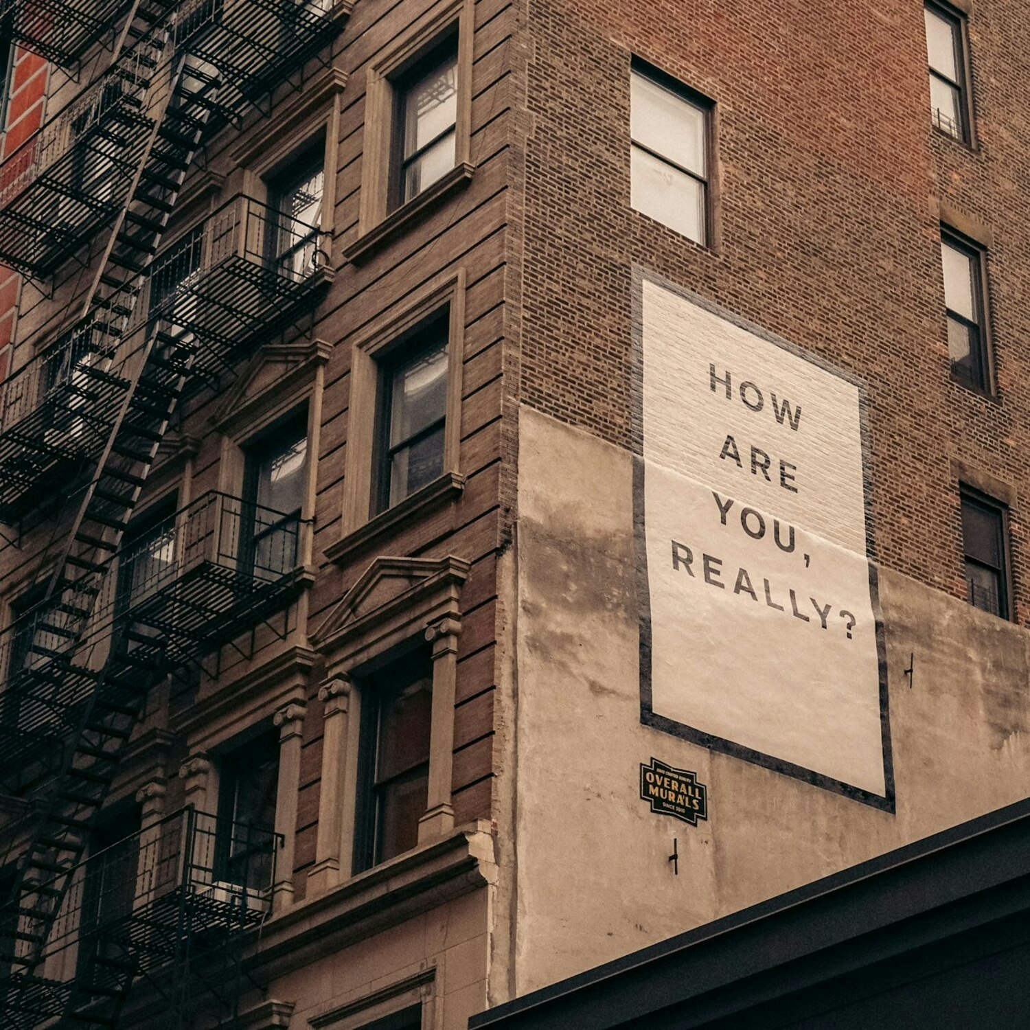 Urban building with fire escape and a large sign asking "HOW ARE YOU, REALLY?"