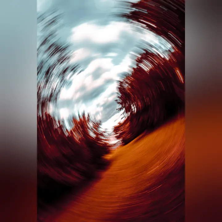 A blurred, swirling photo likely of a forest path with a red-brown ground and trees against the sky, creating a vortex effect.