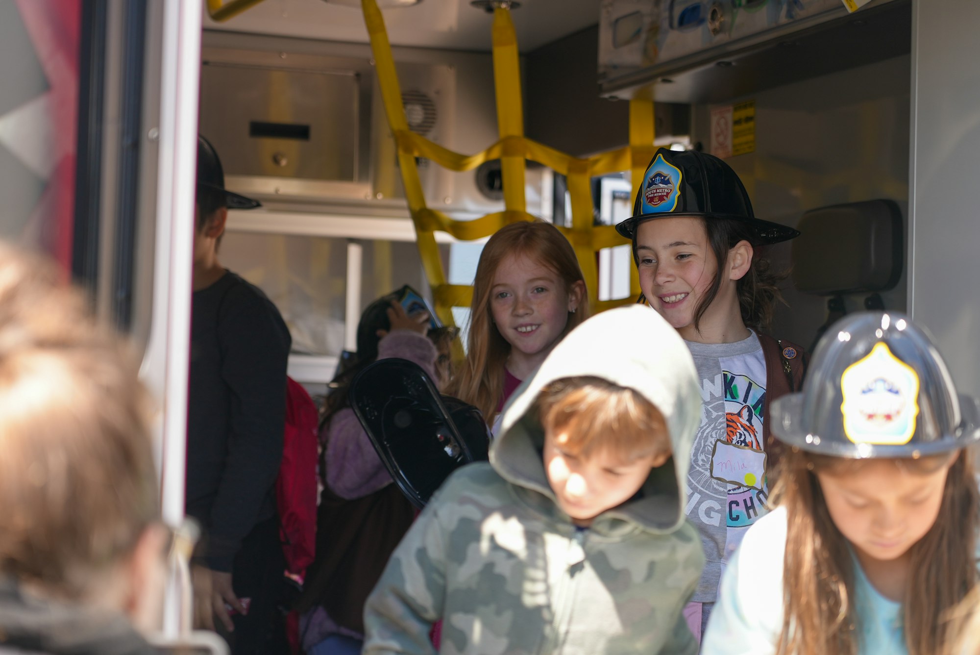 A group of children are inside a vehicle, some wearing hats and smiling, suggesting a fun outing or educational visit.
