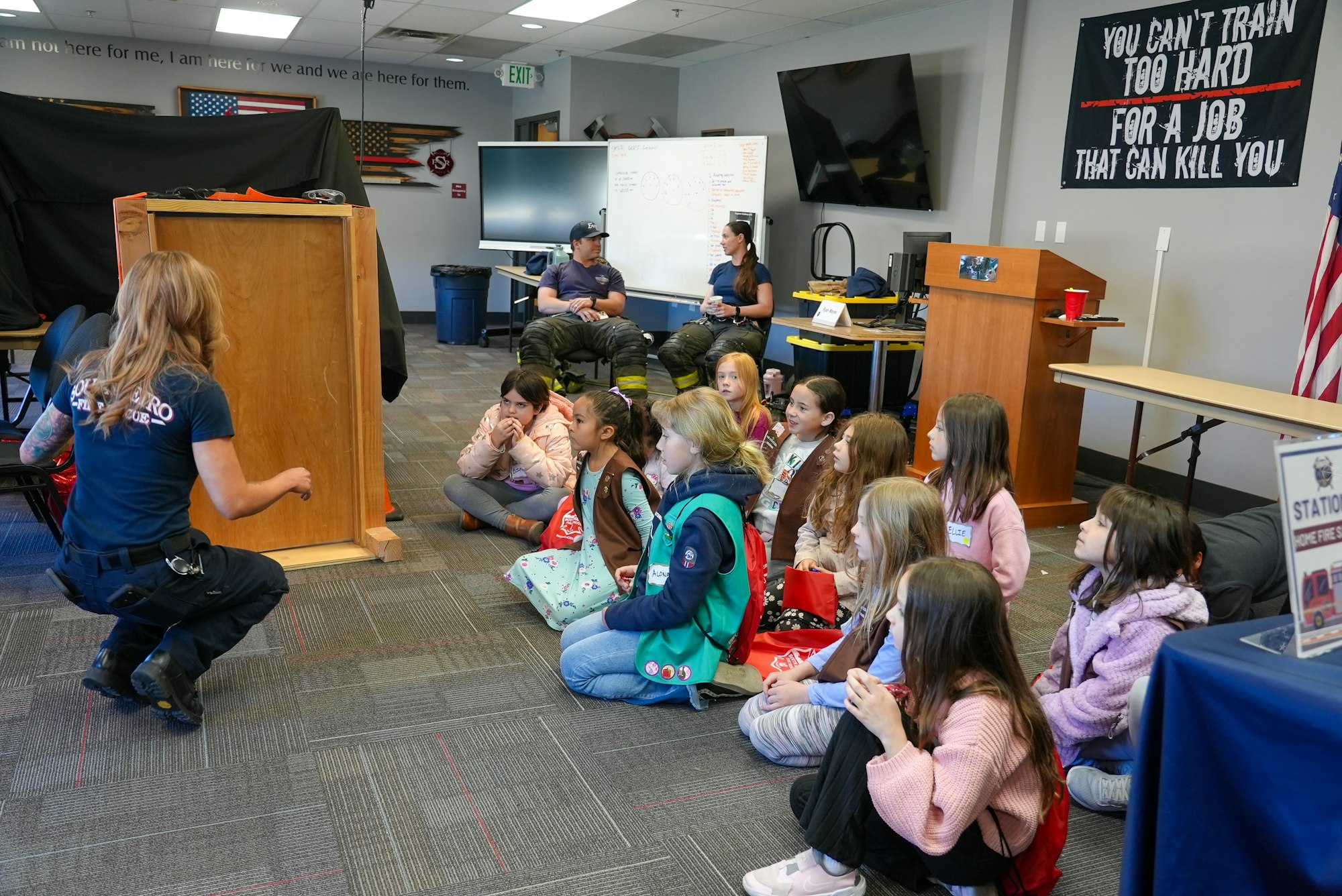 A group of children attentively listening to a speaker at a fire safety presentation in a classroom setting.