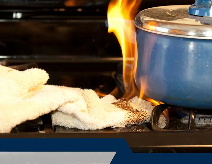 A towel is on fire under a blue pot on a stovetop.
