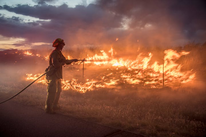 A firefighter battles a raging wildfire at twilight.