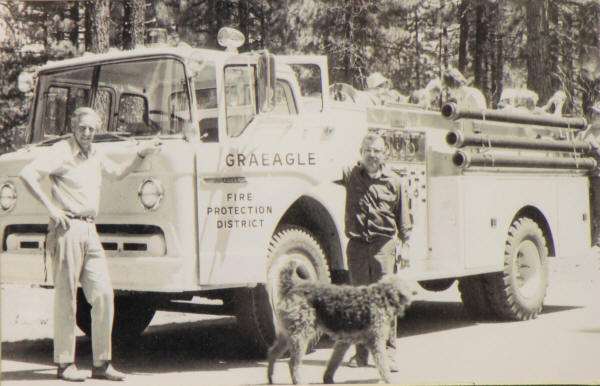 Two people and a dog in front of a "Graeagle Fire Protection District" fire truck.